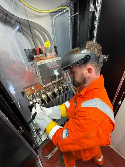 Electric technician in blue hard hat fixing electrical wiring in control box